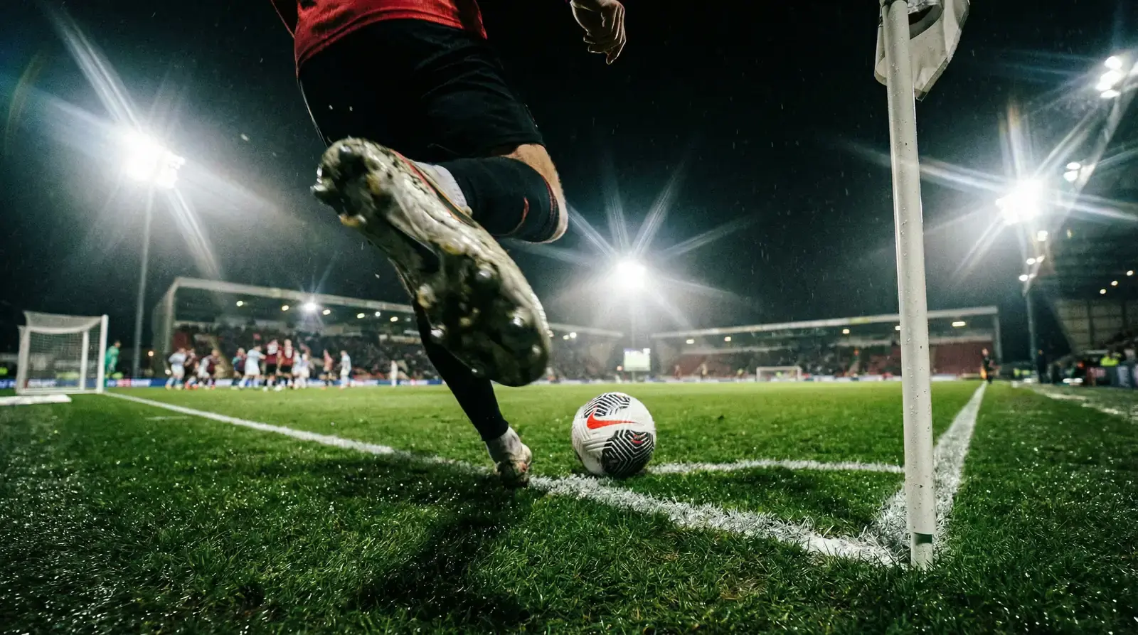 Pontapé de canto num campo de futebol relvado durante um jogo noturno com holofotes